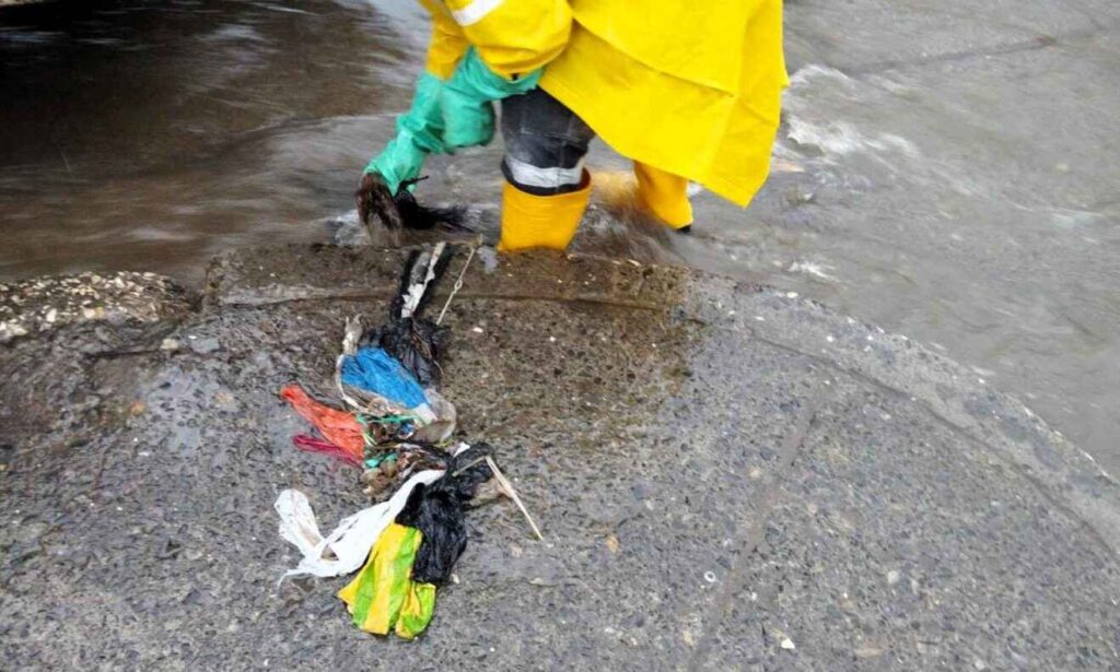 Personal municipal mientras retira basura de los sumideros, que provocan inundaciones.