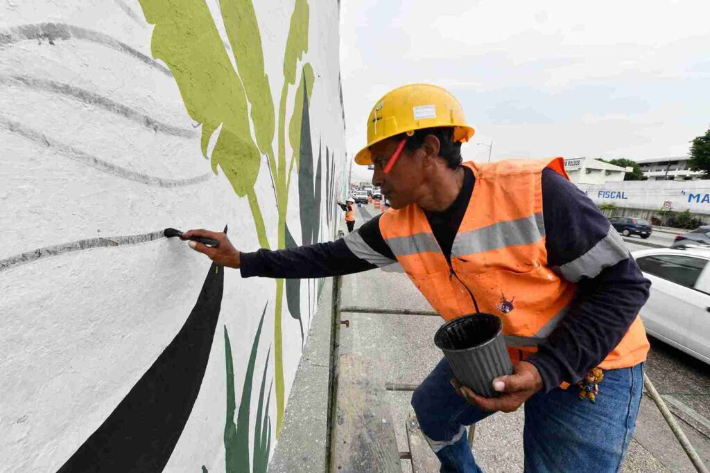 Un trabajador de la cuadrilla de pintura de la Dirección de Obras Públicas, dibuja una planta en el mural. 